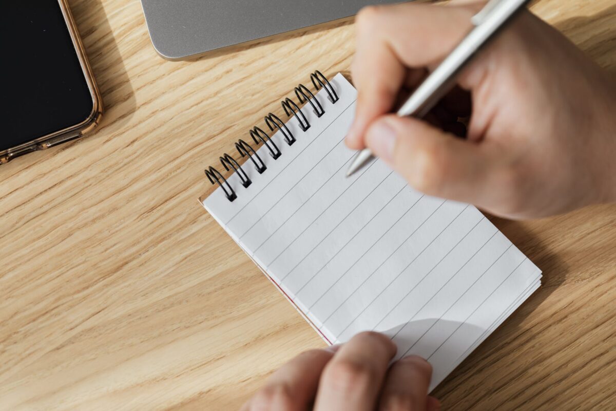 Mans hand writing on a notebook wit ha silver pen