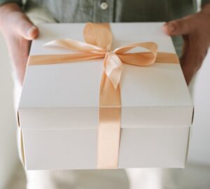 White box with gold ribbon tied into a bow, held by two hands Sentimental Gifts