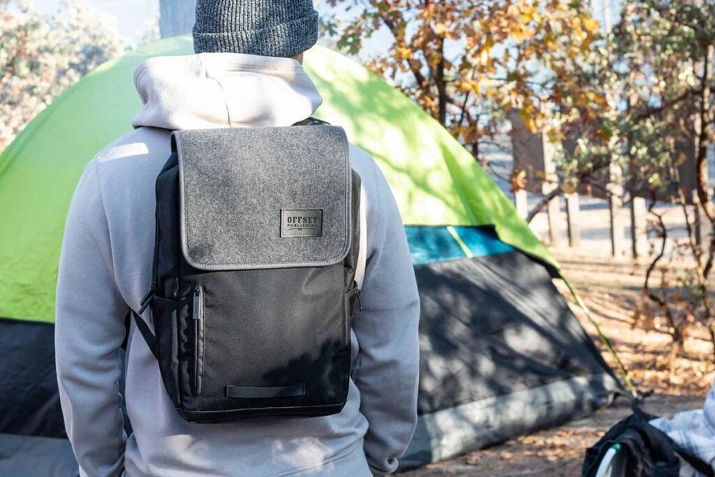 man standing with backpack in front of tent