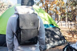 man standing with backpack in front of tent