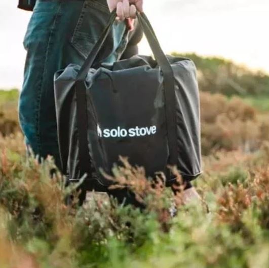 Person carrying solo stove in bag through a field