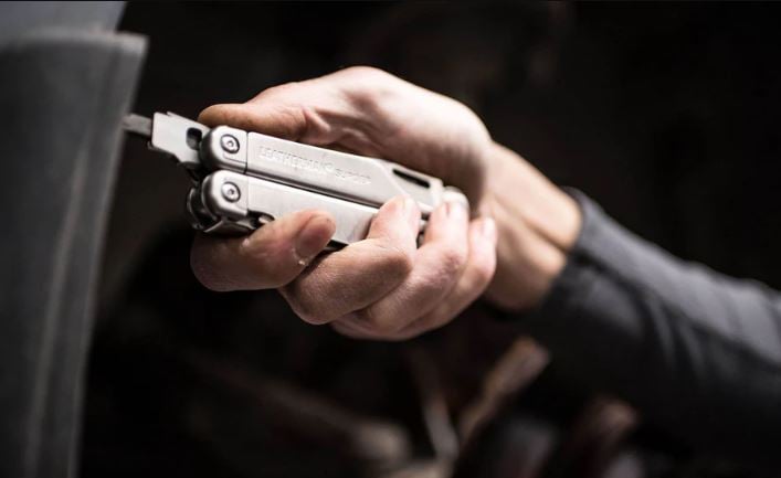 Leatherman surge on dark background with person using it to tighten a screw