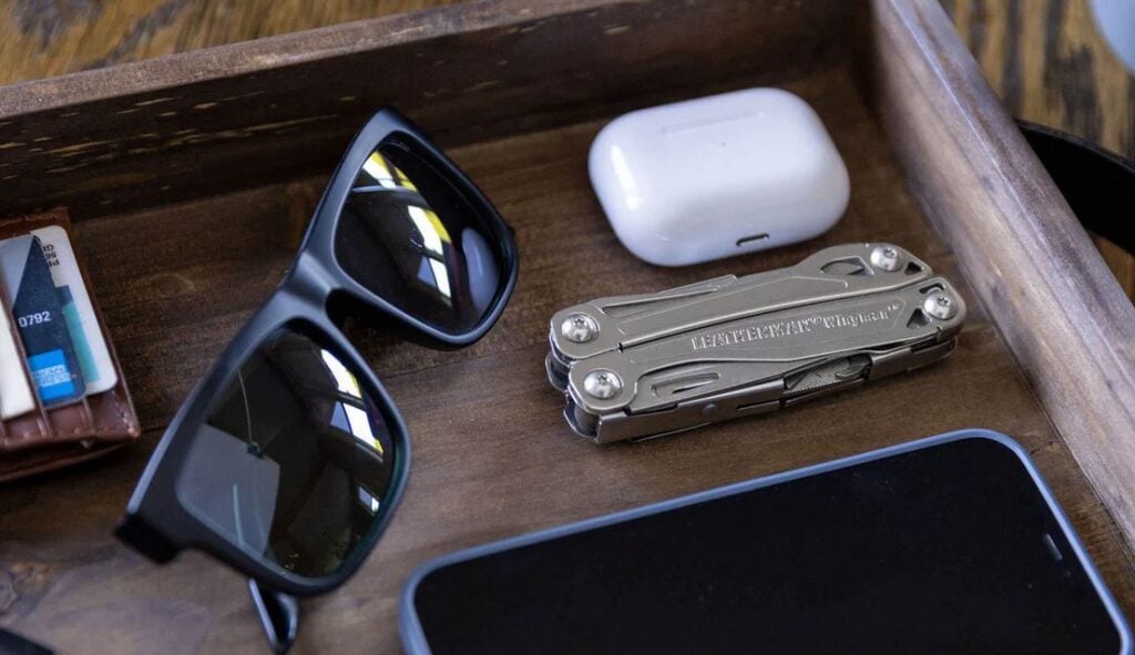 Closed engraved Leatherman wingman next to sunglasses, cell phone, and ear bud case