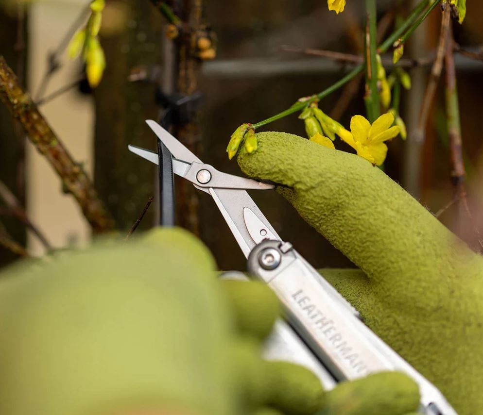 Green glove holding leatherman wave plus multitool using scissors to prune a plant